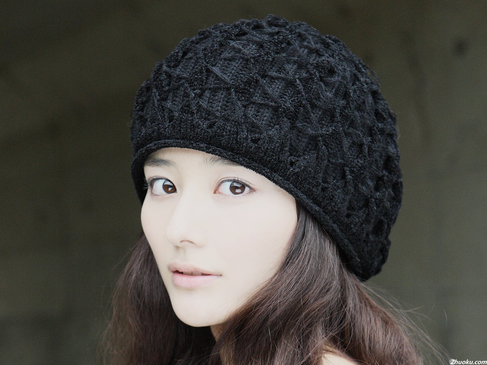 HD desktop wallpaper featuring a mysterious woman with long dark hair wearing a textured black knit hat against a blurred neutral background.