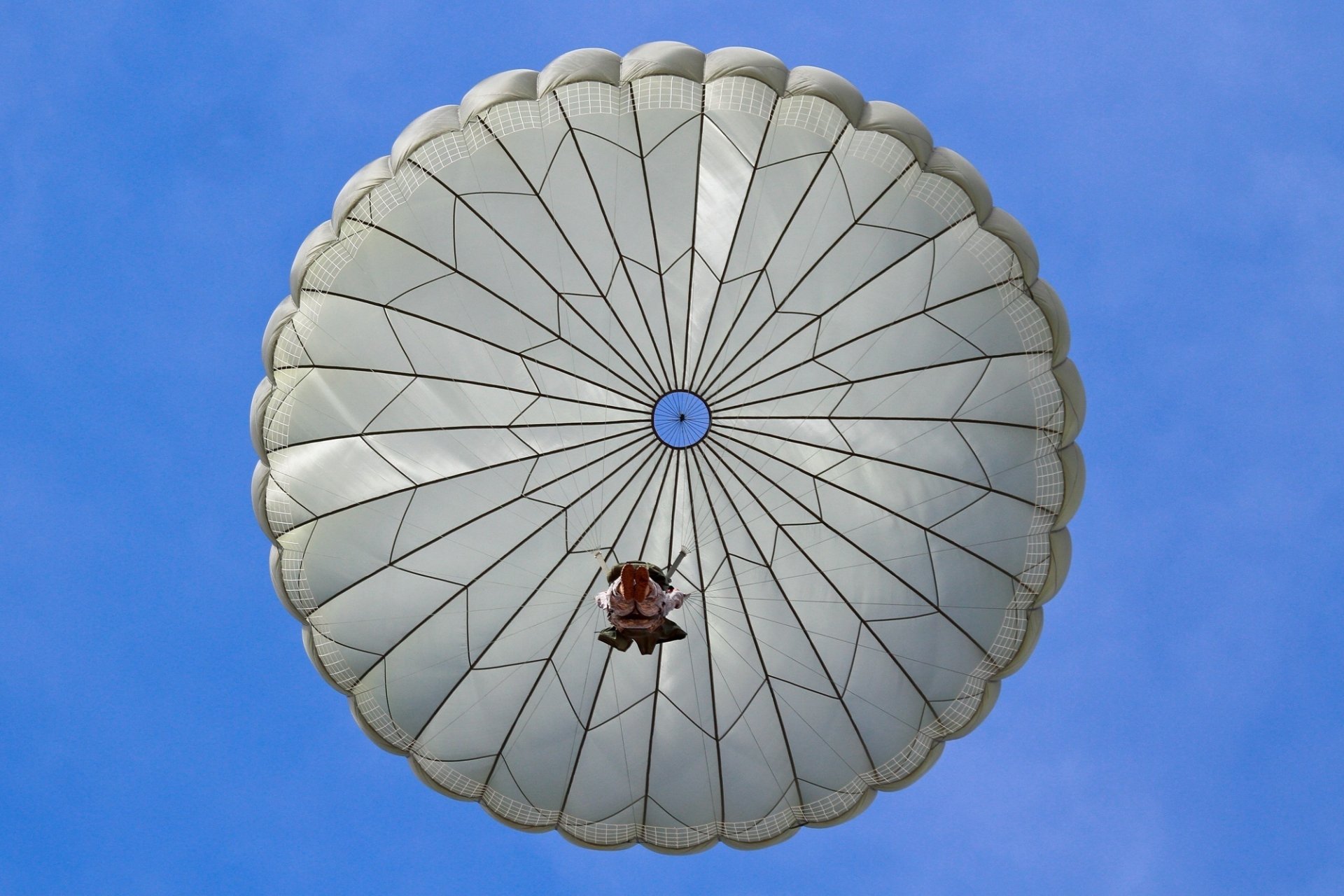 HD desktop wallpaper showing a military paratrooper descending with a fully deployed round parachute against a clear blue sky.