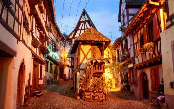 5K Ultra HD desktop wallpaper of historic half-timbered houses on a cobblestone street in Colmar, France, warm evening lights on charming man-made town buildings.