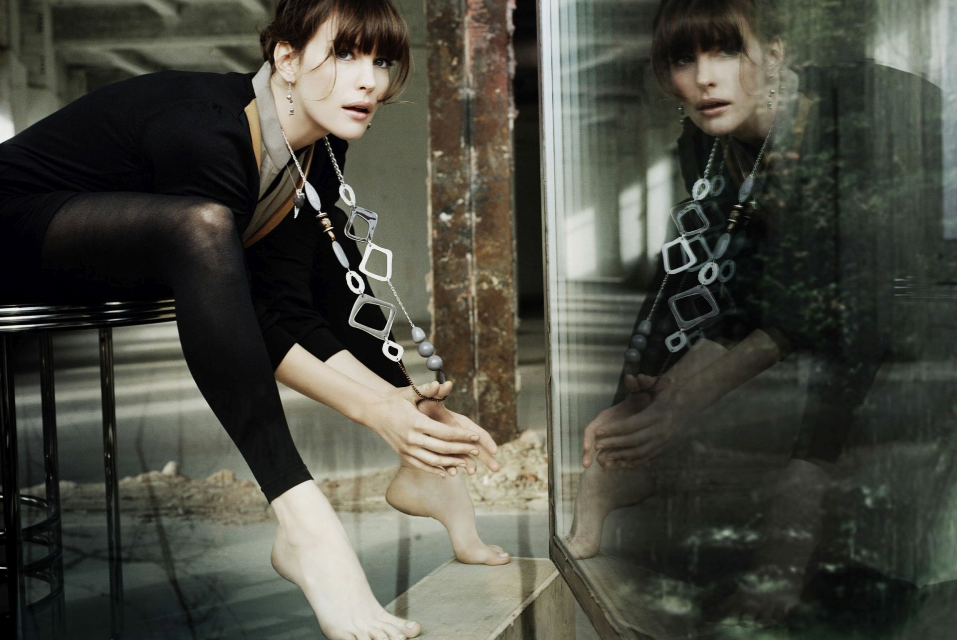 HD desktop wallpaper of brunette actress Liv Tyler, capturing her reflection against a glass surface in a moody, artistic setting.