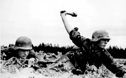 HD desktop wallpaper showing two military soldiers in combat gear, one throwing a grenade while lying in a field.
