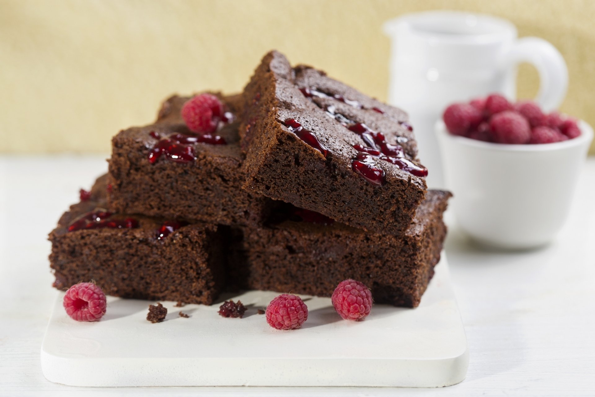 Close-up of rich chocolate brownies topped with raspberries, arranged on a white surface with a blurred background, showcased as an HD PC desktop wallpaper.