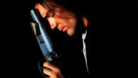 HD PC desktop wallpaper: moody Desperado movie scene showing a man in profile cradling a pistol, his face lit against a deep black background.