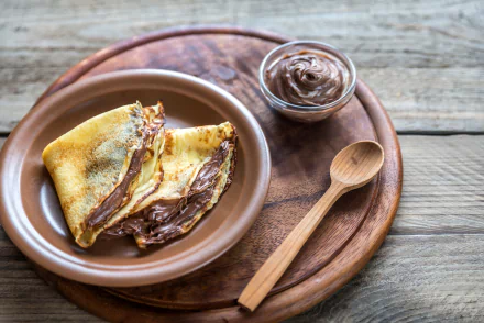 4K Ultra HD PC desktop wallpaper: folded crêpe spread with Nutella on a ceramic plate, small jar of chocolate spread and wooden spoon on a rustic wooden board — food.