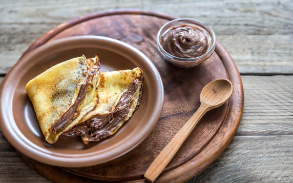 4K Ultra HD PC desktop wallpaper: folded crêpe spread with Nutella on a ceramic plate, small jar of chocolate spread and wooden spoon on a rustic wooden board — food.