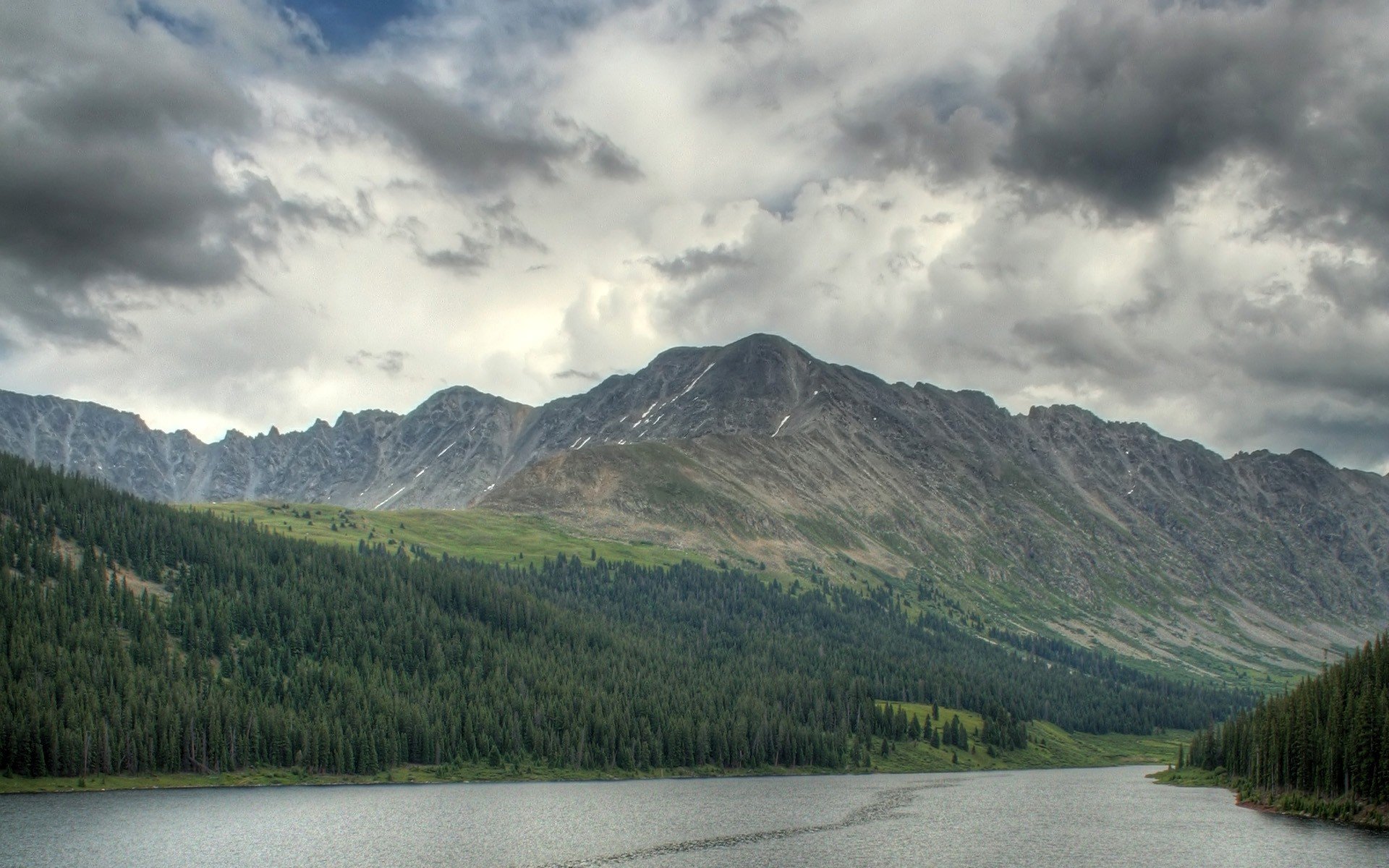A serene landscape featuring a river flowing through a lush forest, framed by mountains under a cloudy sky, capturing the essence of nature and tranquility.
