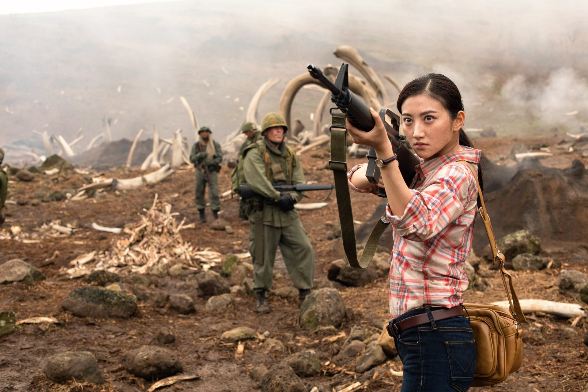 HD desktop wallpaper and background featuring Jing Tian from the movie Kong: Skull Island. She stands in a rugged landscape with soldiers in the background, holding a weapon.