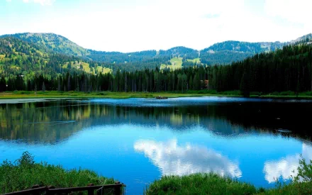A serene HD desktop wallpaper featuring a tranquil lake with a dock and boat, surrounded by lush trees, a cabin, and mountains under a bright sky, capturing the peaceful essence of nature and landscape photography.