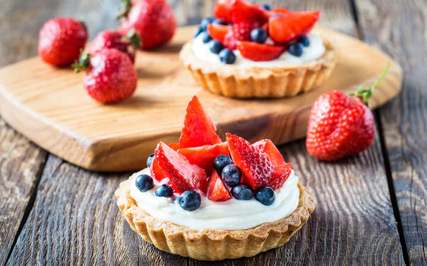 A 4K Ultra HD still life of a blueberry and strawberry tart dessert on a rustic wooden surface with fresh berries scattered around.