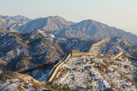 A breathtaking view of the Great Wall of China amidst snow-covered mountains, showcasing the contrast of man-made architecture and natural winter beauty in stunning 4K Ultra HD.