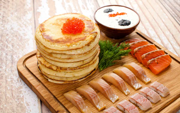 HD desktop wallpaper featuring a stack of pancakes topped with caviar, accompanied by seafood slices, smoked salmon, and a bowl of sour cream with caviar on a wooden board.