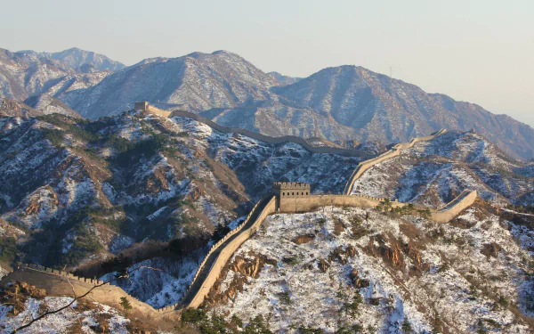 A breathtaking view of the Great Wall of China amidst snow-covered mountains, showcasing the contrast of man-made architecture and natural winter beauty in stunning 4K Ultra HD.