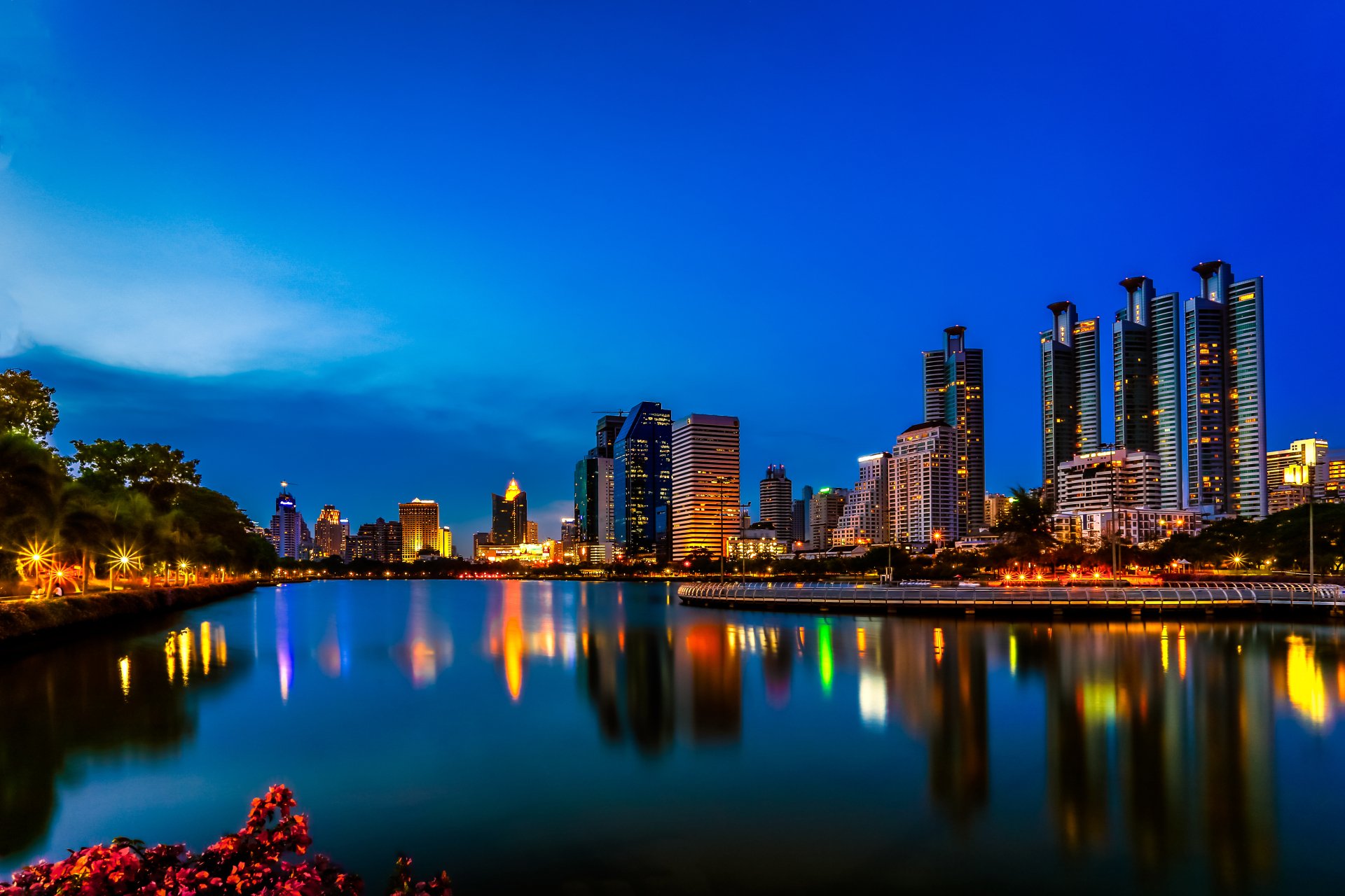 Nighttime cityscape of Bangkok, Thailand featuring illuminated skyscrapers reflecting on a calm lake, captured in 4K Ultra HD as a vibrant man-made urban scene.