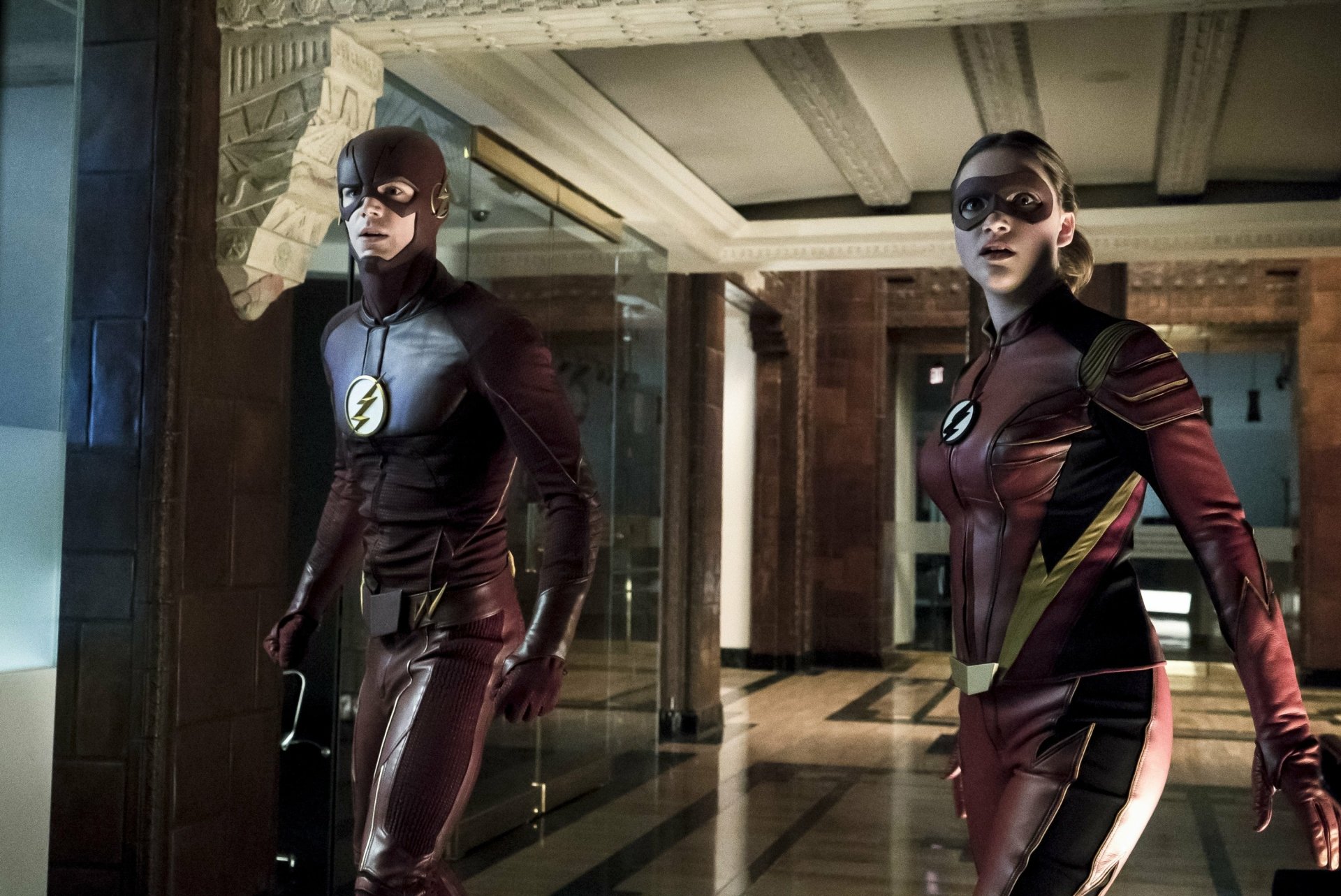HD wallpaper featuring Barry Allen (Grant Gustin) and Jesse Quick (Violett Beane) in costume from the TV show The Flash (2014), inside a dimly lit, modern building.