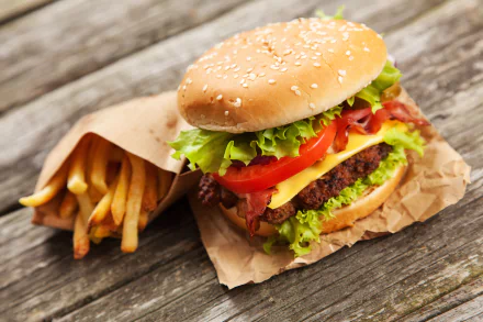 4K Ultra HD desktop wallpaper featuring a close-up of a juicy burger with lettuce and tomato, accompanied by crispy golden french fries on rustic wooden surface.