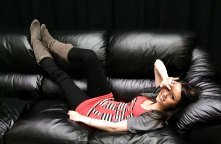 A cute, smiling Miley Cyrus lounges comfortably on a black leather couch, her playful pose and stylish outfit creating a lively and inviting HD desktop wallpaper.