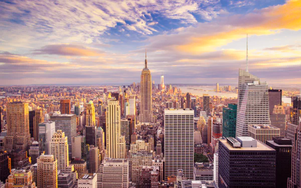 A stunning HD cityscape wallpaper featuring the horizon of New York City with the iconic Empire State Building and numerous skyscrapers set against a vibrant sky.