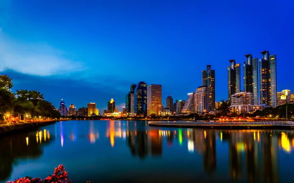 Nighttime cityscape of Bangkok, Thailand featuring illuminated skyscrapers reflecting on a calm lake, captured in 4K Ultra HD as a vibrant man-made urban scene.