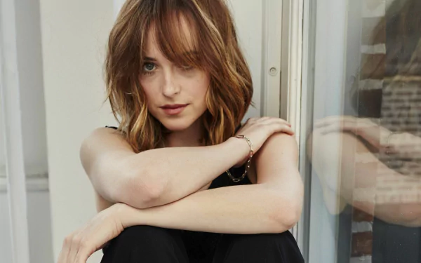 HD desktop wallpaper featuring actress Dakota Johnson in a thoughtful pose, showcasing her natural beauty with soft lighting and a neutral background.