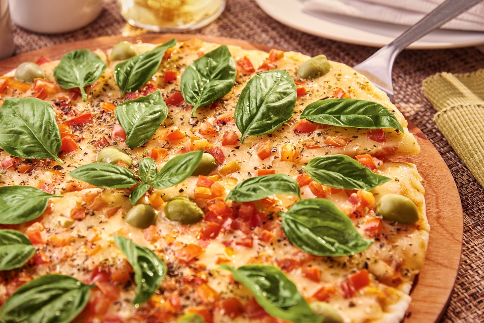 Still-life food photo of a basil-topped pizza with green olives, diced tomatoes and melted cheese on a wooden board — 2K Quad HD PC desktop wallpaper and background.