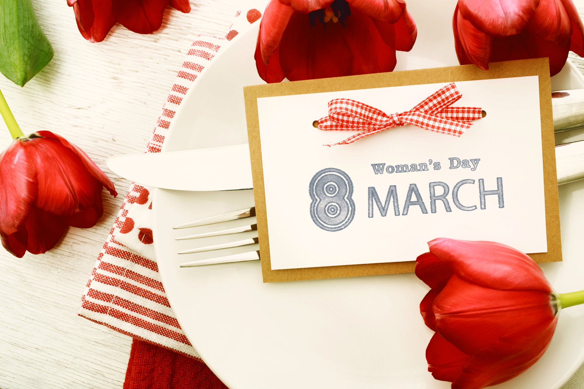 A beautiful arrangement featuring vibrant red tulips, a festive table setting, and a card celebrating Women's Day on March 8, all crafted for a striking 4K Ultra HD desktop wallpaper.