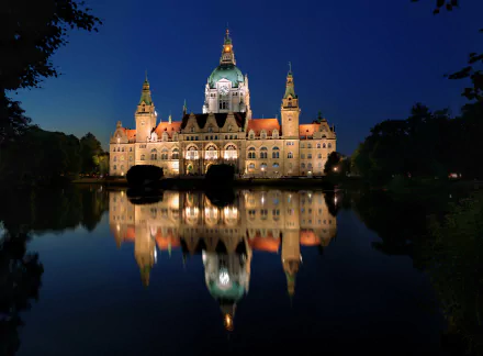The HD desktop wallpaper shows the illuminated New Town Hall in Hanover, Germany at night, beautifully reflected in the lake. The building stands majestically against the dark sky, creating a stunning night scene.