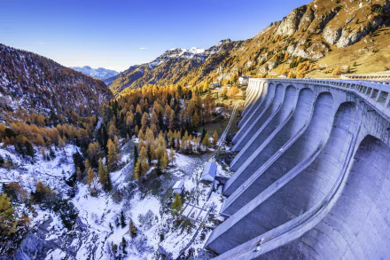HD PC desktop wallpaper and background: man-made concrete dam curving through a snowy mountain winter landscape, golden trees and a clear blue sky.