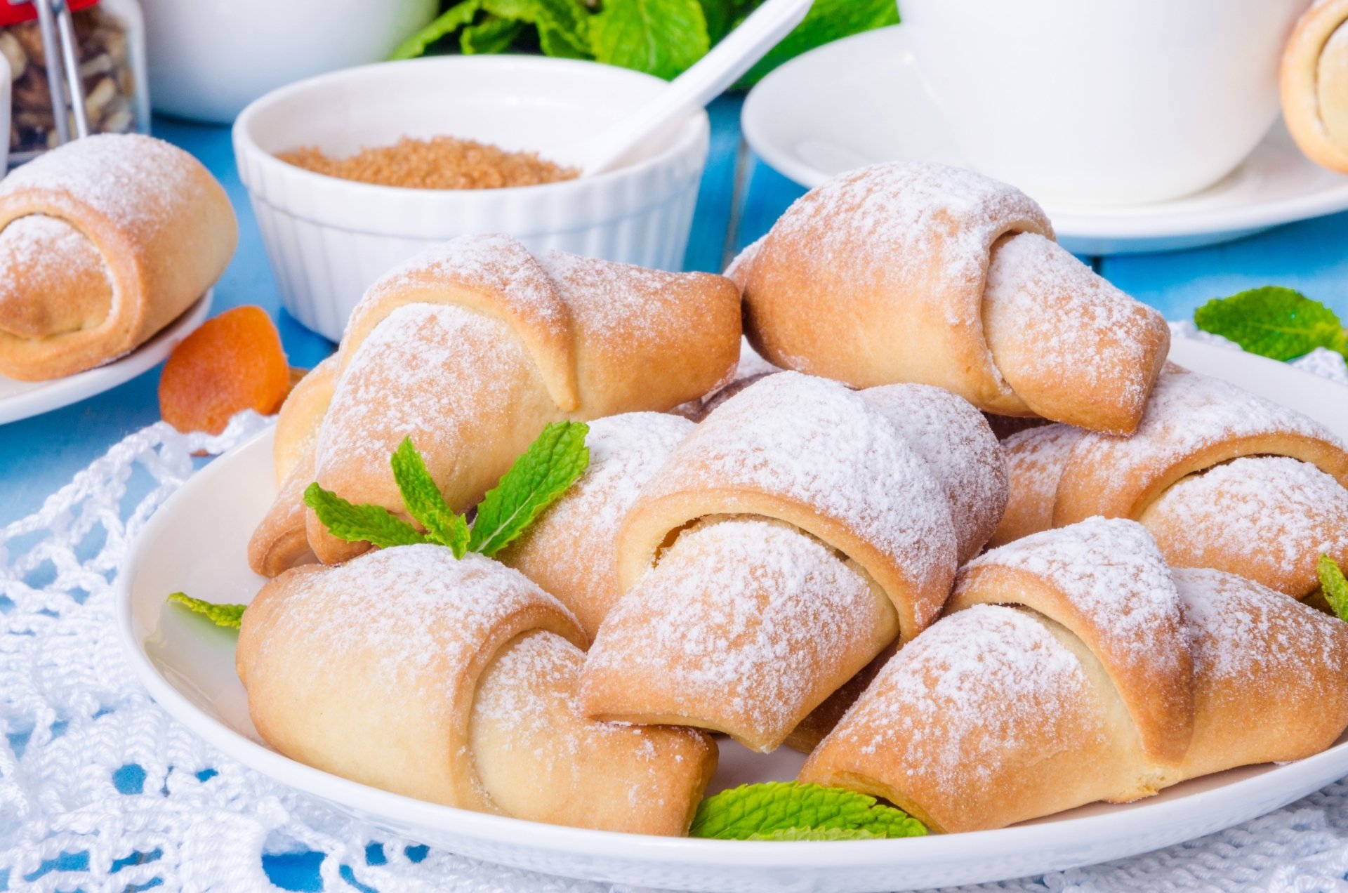 2K Quad HD PC desktop wallpaper and background: breakfast food—plate of powdered-sugar croissants garnished with mint on a lace doily, bowls and a cup softly blurred behind.