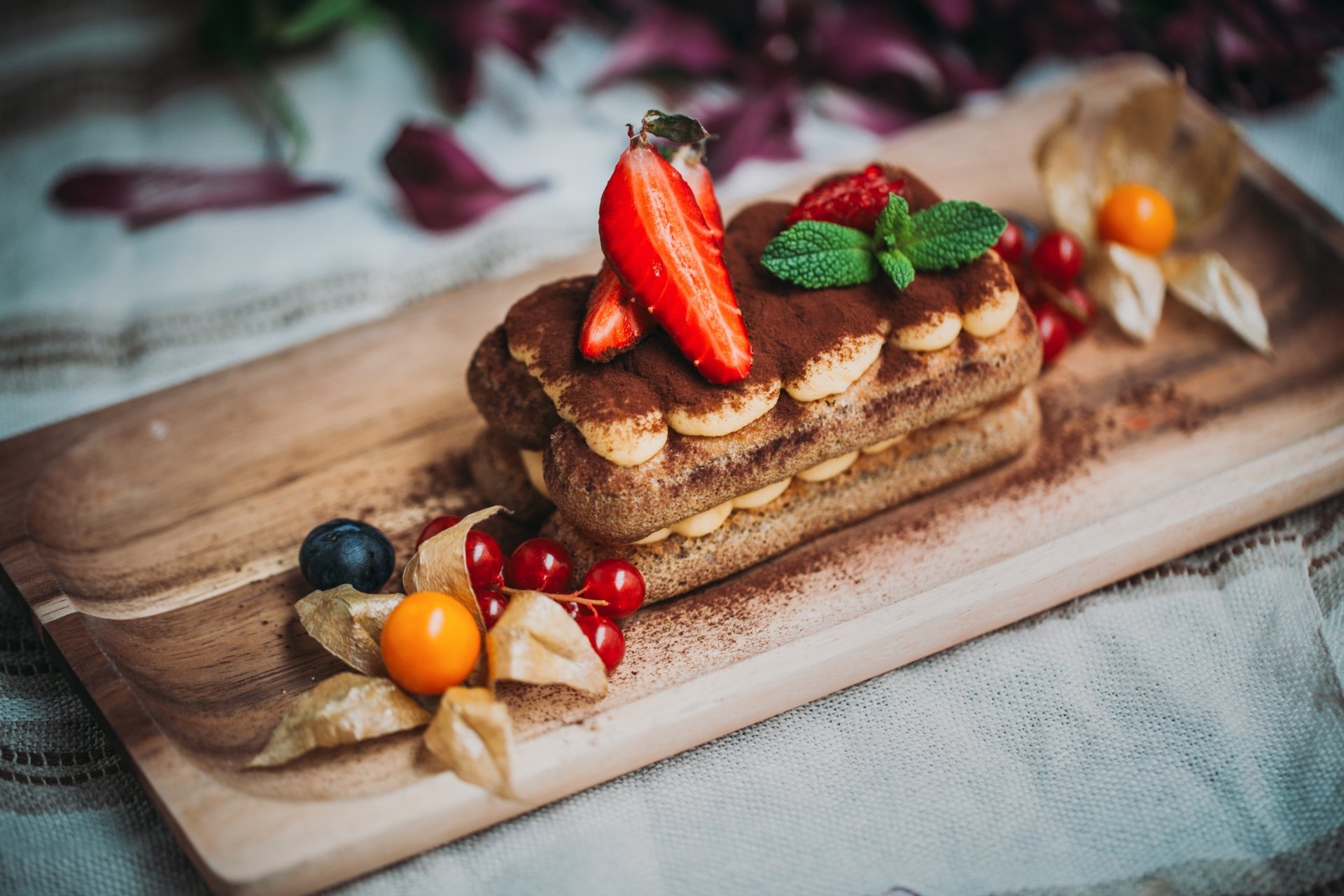 2K Quad HD PC desktop wallpaper: close-up of a layered pastry dessert on a wooden board, garnished with sliced strawberries, mint and mixed berries — food pastry background.