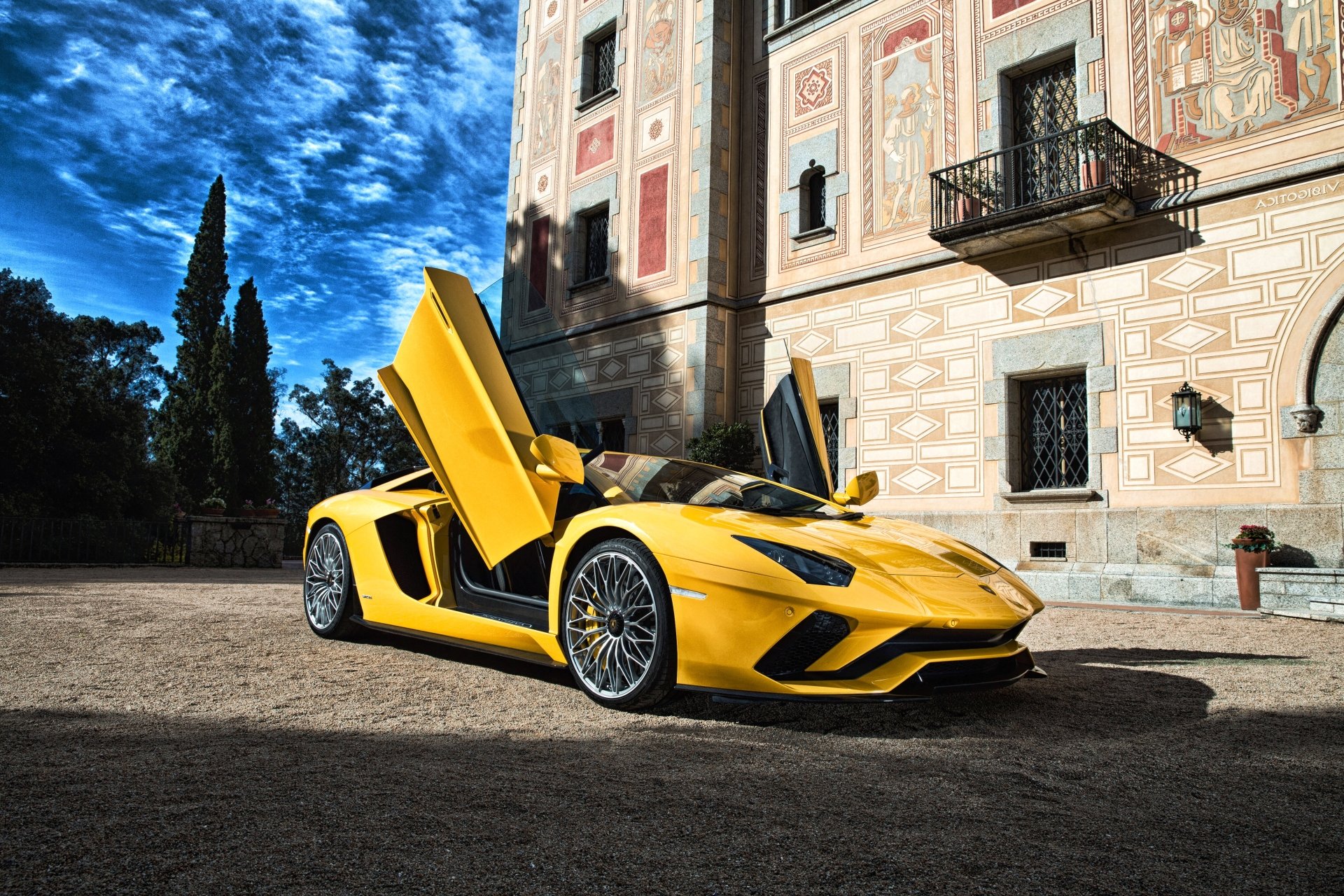 Yellow Lamborghini Aventador S supercar (yellow car) with scissor doors open, parked before an ornate building under a dramatic blue sky — 4K Ultra HD desktop wallpaper of the vehicle.