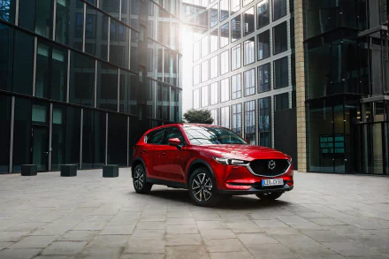 Red Mazda CX-5 SUV parked in a glass-clad urban plaza with sunlight reflections — 2K Quad HD PC desktop wallpaper background.