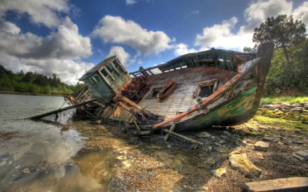 A striking HD desktop wallpaper of a wrecked boat resting on the shore, surrounded by water and trees, under a dramatic sky filled with clouds.