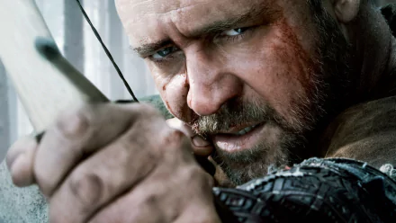 Close-up of Russell Crowe as Robin Hood from the 2010 movie, aiming a bow and arrow with intense focus in this HD PC desktop wallpaper.