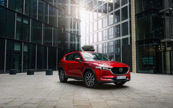Red Mazda CX-5 SUV parked in a glass-clad urban plaza with sunlight reflections — 2K Quad HD PC desktop wallpaper background.