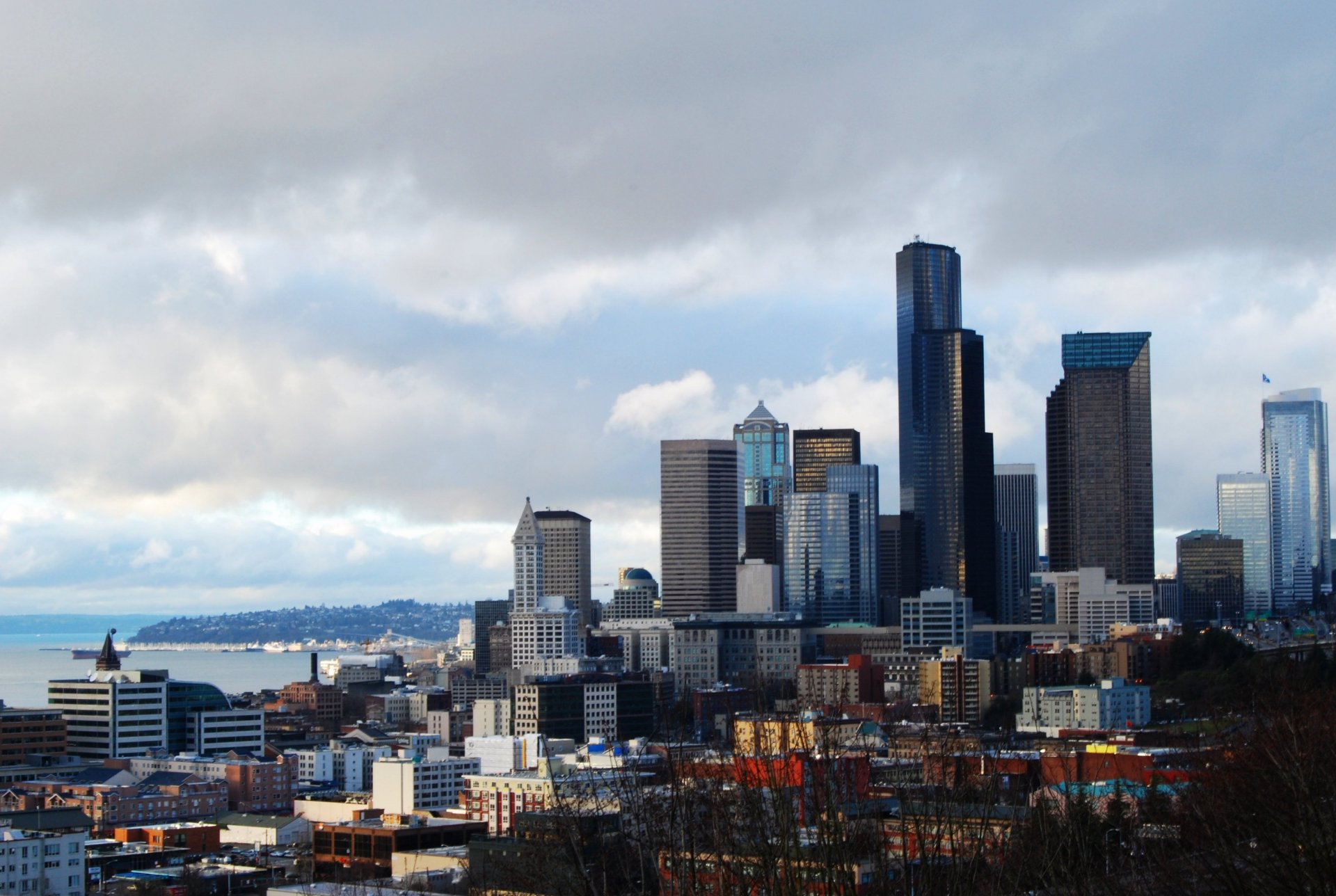 Seattle man-made skyline under moody clouds — 2K Quad HD PC desktop wallpaper showing downtown skyscrapers and the Elliott Bay waterfront.
