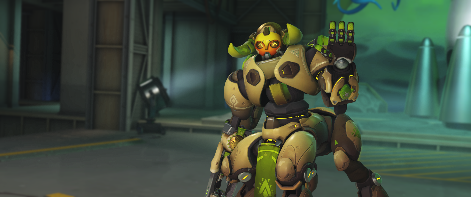 HD PC desktop wallpaper of Orisa from Overwatch: armored green-and-gold omnic guardian in a hangar, raising a hand with a weapon at her side, video game artwork background.