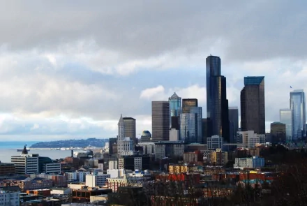 Seattle man-made skyline under moody clouds — 2K Quad HD PC desktop wallpaper showing downtown skyscrapers and the Elliott Bay waterfront.