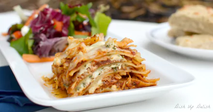 HD desktop wallpaper featuring a close-up of a layered lasagna meal served on a white plate with a side salad and bread in the background.