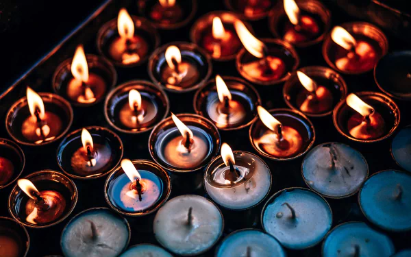 Close-up 4K Ultra HD wallpaper of numerous lit candles with bright flames, showcasing warm orange and yellow tones in a dark setting.