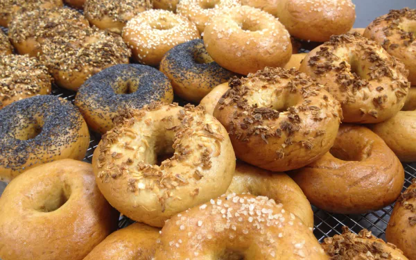HD PC desktop wallpaper of assorted bagels and bread—sesame, poppy, onion and plain—stacked on a rack as a food background.