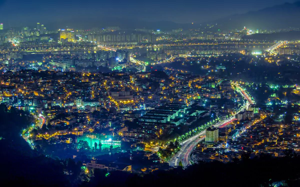 HD wallpaper featuring a vibrant night cityscape of Seoul, South Korea, with colorful city lights illuminating the urban landscape and creating a mesmerizing view.