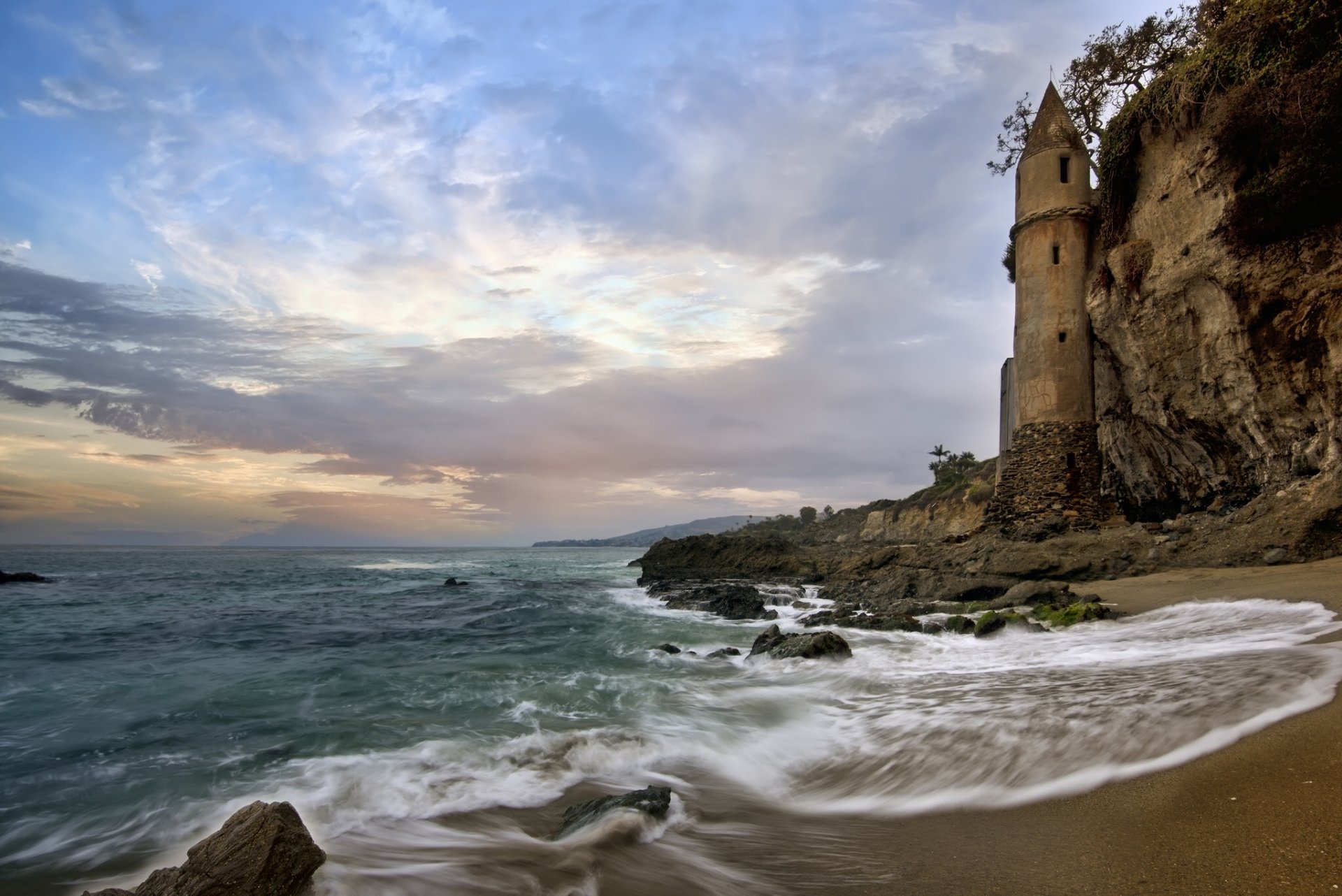 Laguna Beach, California sunset on the ocean horizon: rocky shoreline with cliff tower and sweeping sand — HD PC desktop wallpaper background.
