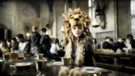 Luna Lovegood, adorned in a whimsical lion hat, sits at the Gryffindor table during a scene from Harry Potter and the Half-Blood Prince. HD wallpaper captures the magical atmosphere.