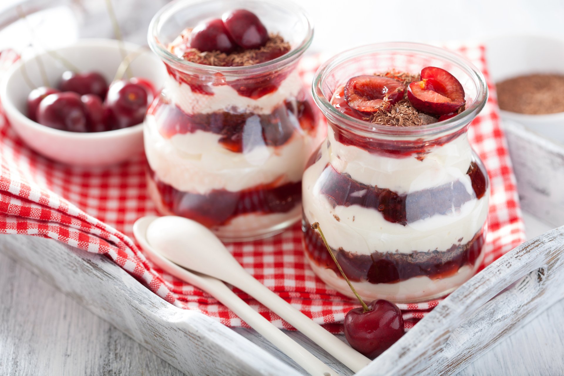 5K Ultra HD PC desktop wallpaper of a cherry yogurt dessert (food): two glass jars layered with yogurt, cherry compote and fresh cherries on a red-checkered cloth.