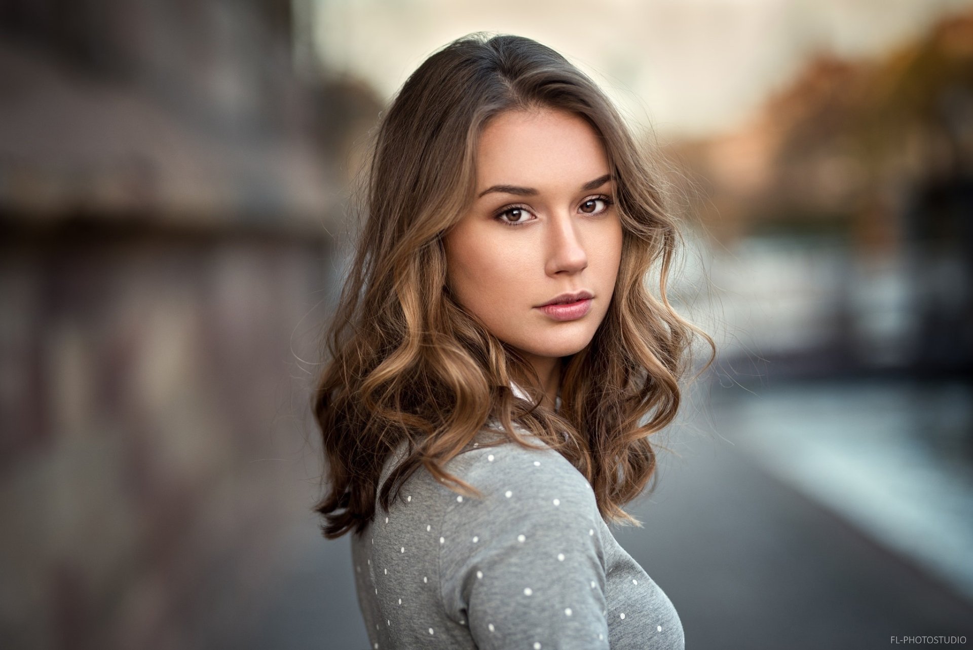 A brunette woman with brown eyes poses outdoors, with a soft depth of field effect highlighting her features. This HD desktop wallpaper captures a serene and focused expression on the model's face.