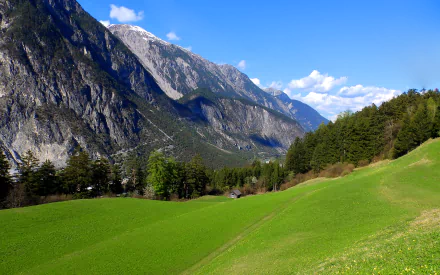 HD desktop wallpaper showcasing a vibrant green field leading to majestic mountains under a bright blue sky, capturing the beauty of nature and landscape.