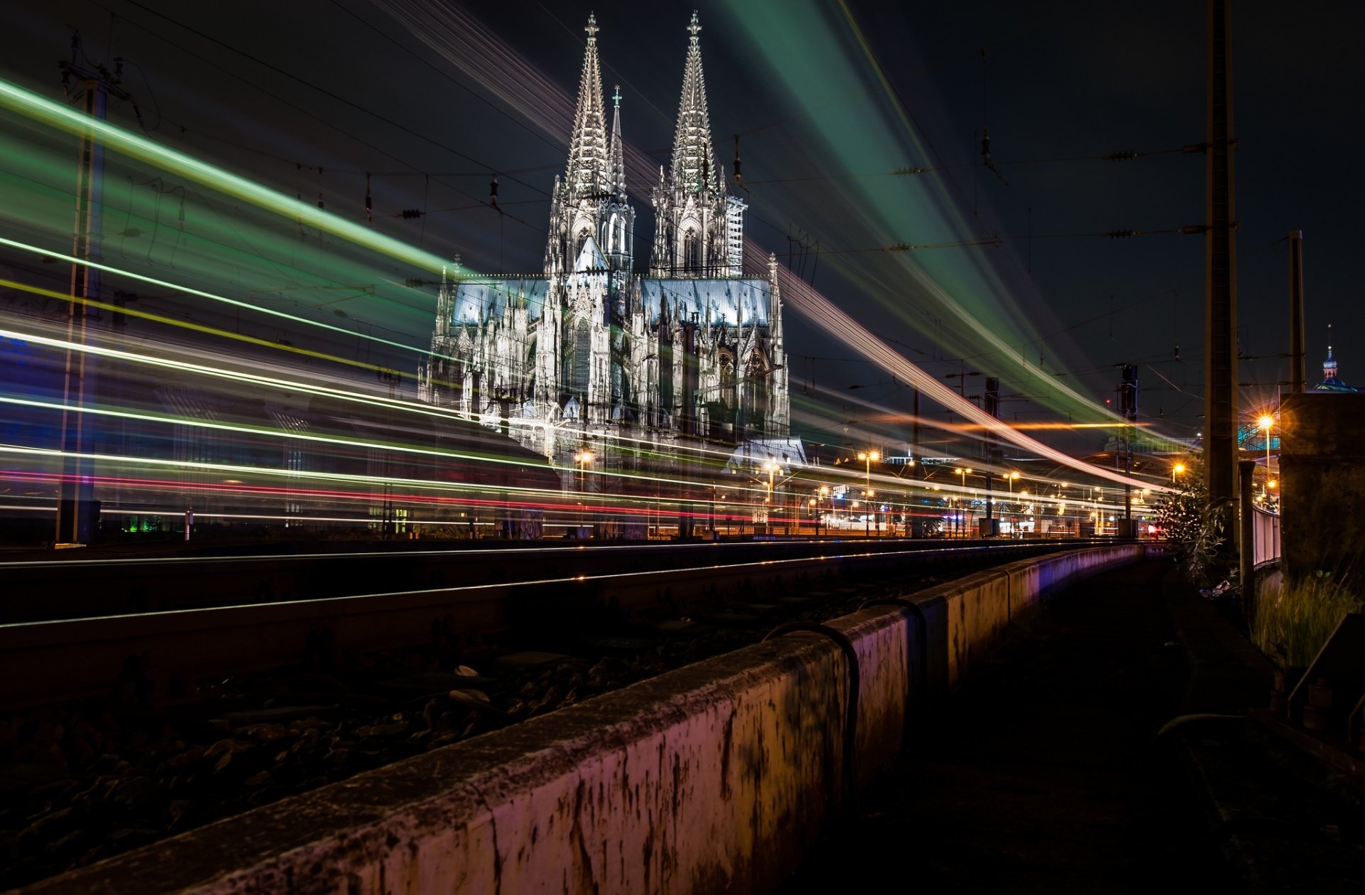 Time-lapse night view of Cologne Cathedral in Germany, showcasing its religious gothic architecture with vibrant light trails in an HD desktop wallpaper.