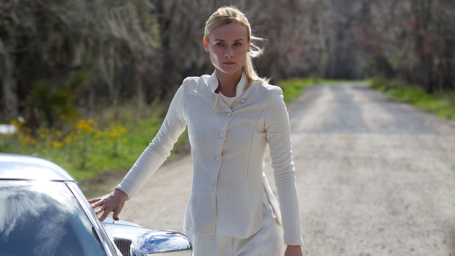 HD desktop wallpaper: still from the movie The Host (2013) showing a woman in a white jacket standing by a car on a sunlit rural road.
