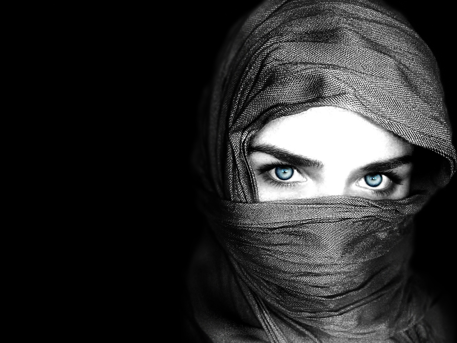 Striking blue eyes of a person covered with a grey headscarf against a black background, perfect for an HD desktop wallpaper.