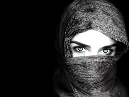 A striking HD desktop wallpaper featuring a woman with captivating blue eyes, partially concealed by a dark scarf against a black background.